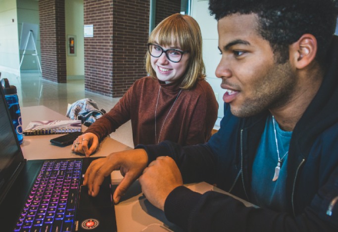 Two students collaborate around a laptop